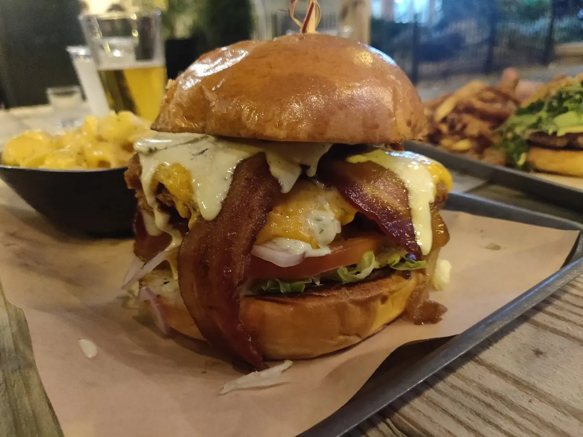 A bacon and egg cheeseburger on a dark table with a beer behind it