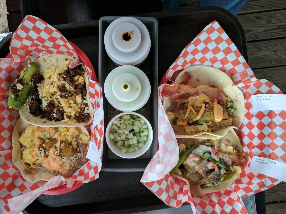 Two soft tacos in checkered paper boats with salsa cups